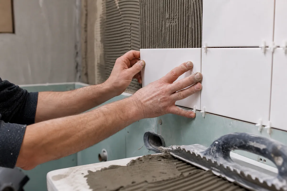 Pose de faïence murale en cours avec croisillons dans une salle de bain en rénovation